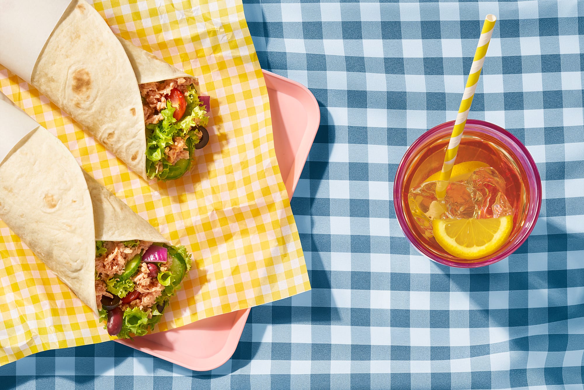 Zwei lecker angerichtete Thunfisch Wraps mit Gurken, Zwiebeln, Oliven, Tomaten, Kidneybohnen und Salat, daneben ein Glas mit Eistee, Ansicht von oben