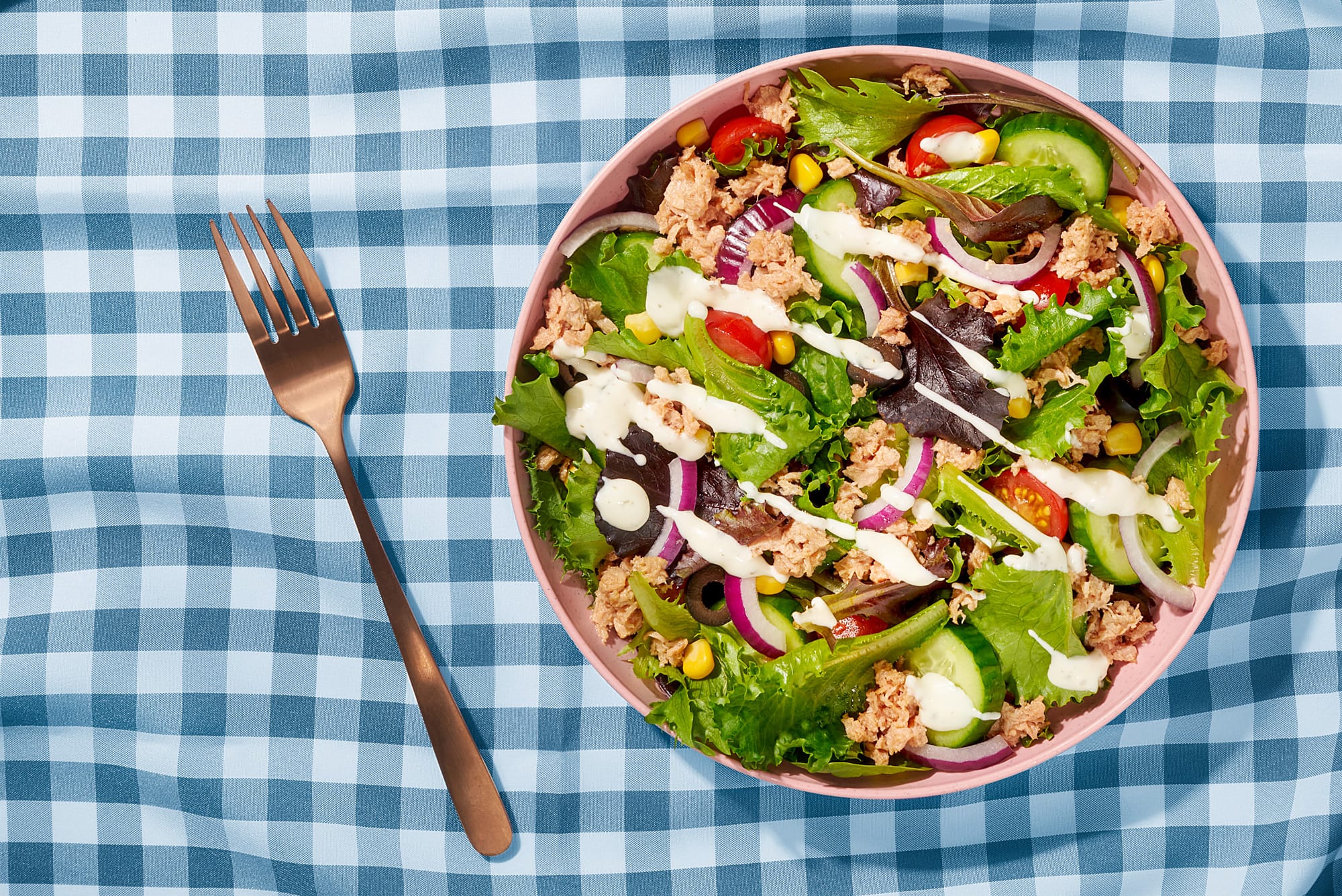 Lecker angerichtete Bowl mit Thunfisch, Gurken, Tomaten, Mais, Zwiebeln, Salat und etwas Dressing, Ansicht von oben